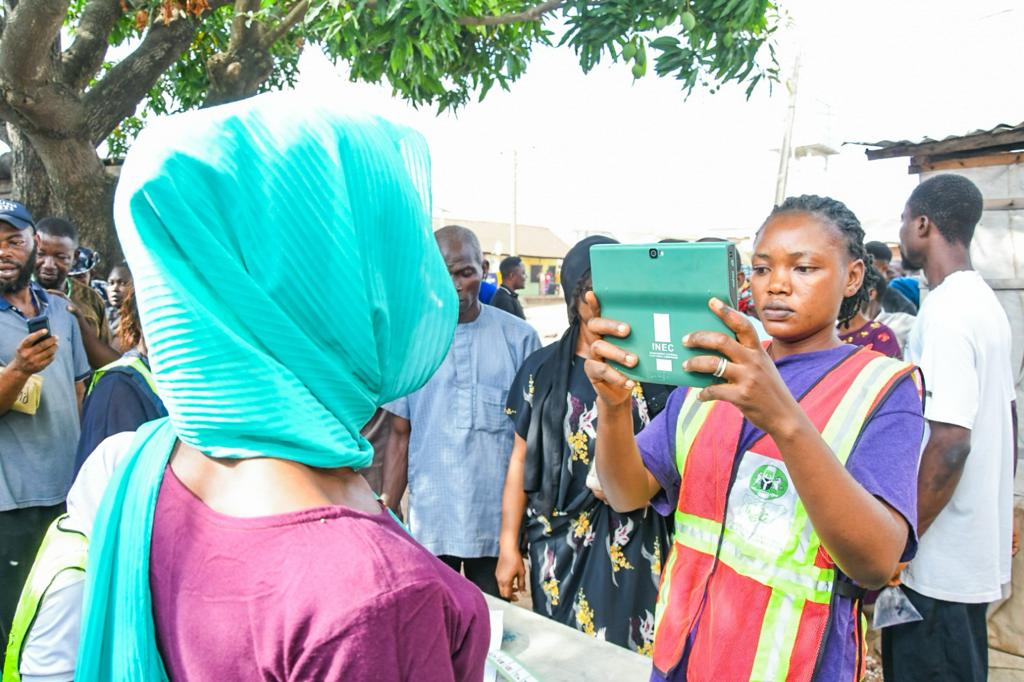 A woman wearing a hijab poses to be captured by an election officer using a tablet
